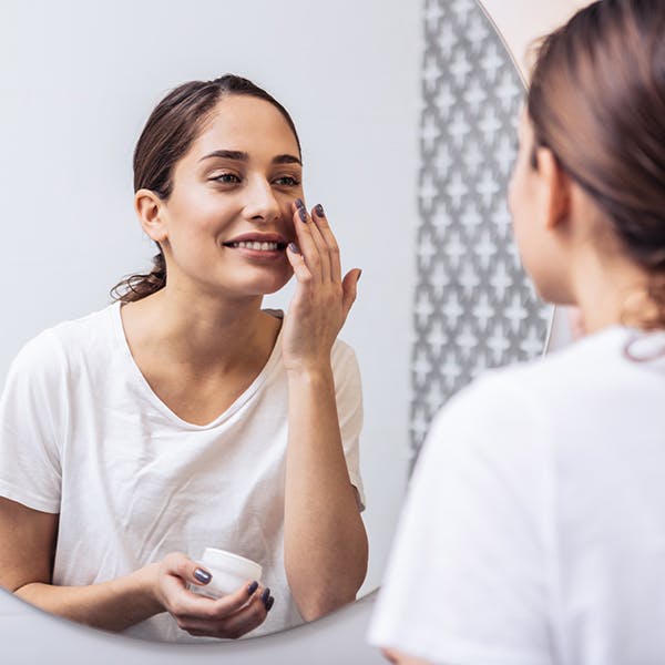 Woman looking in the mirror to apply lotion. 