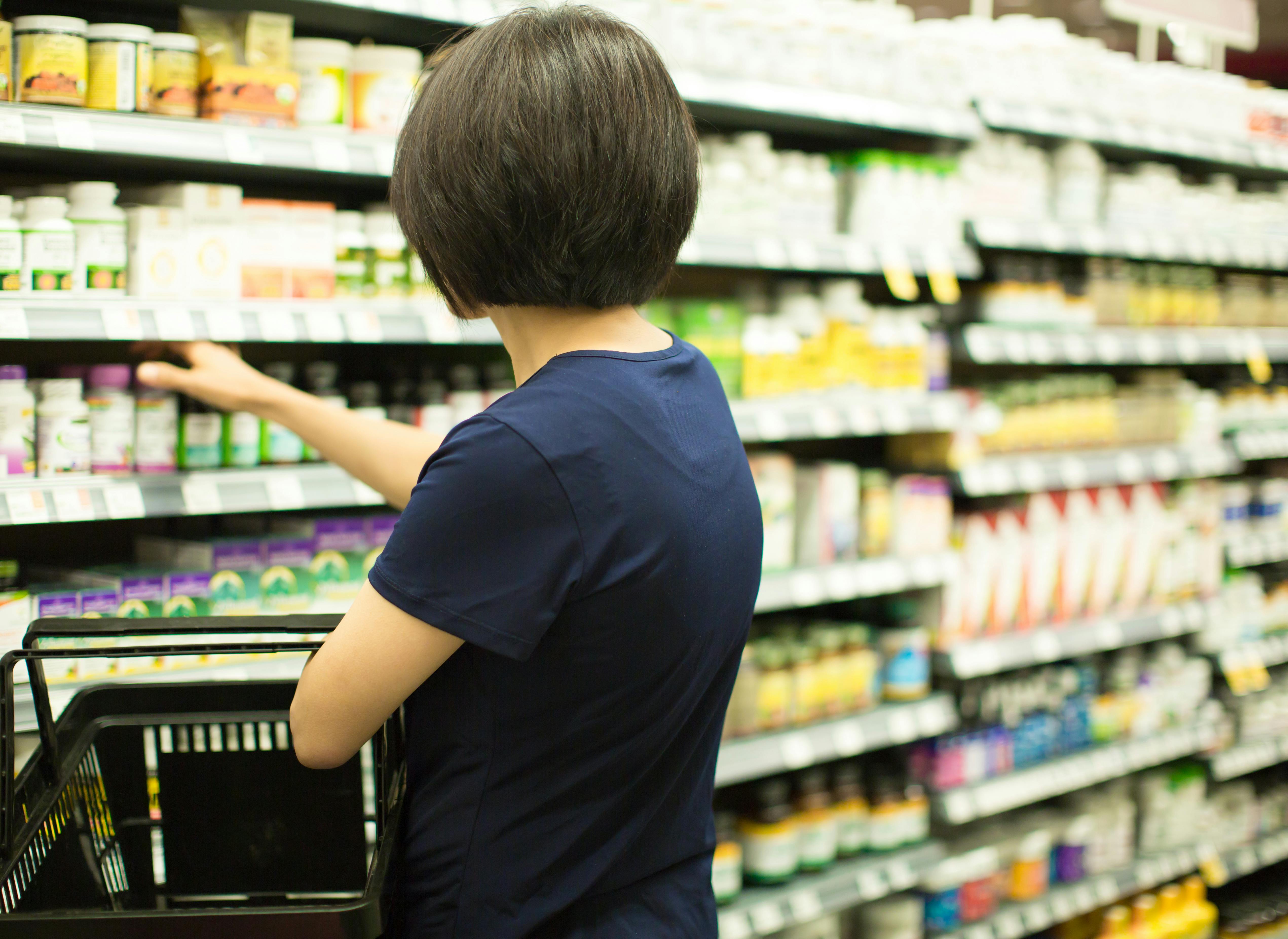 A woman selecting a bottle of vitamins from a store’s shelf.