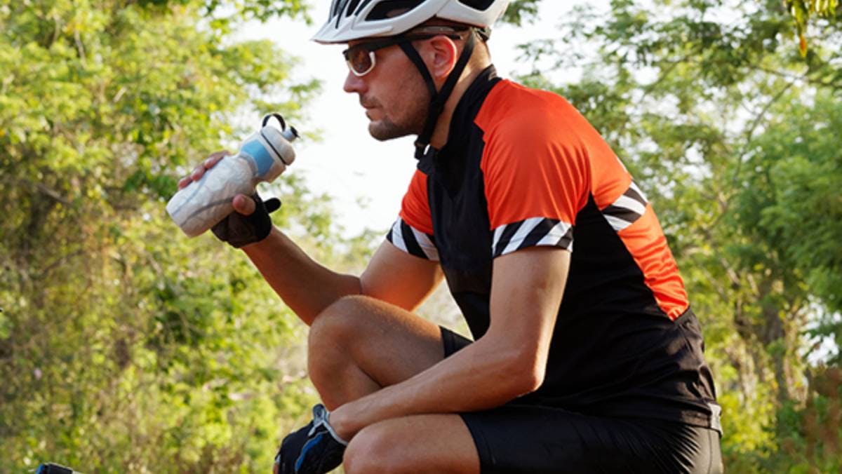 Man drinking water while crouching near bicycle