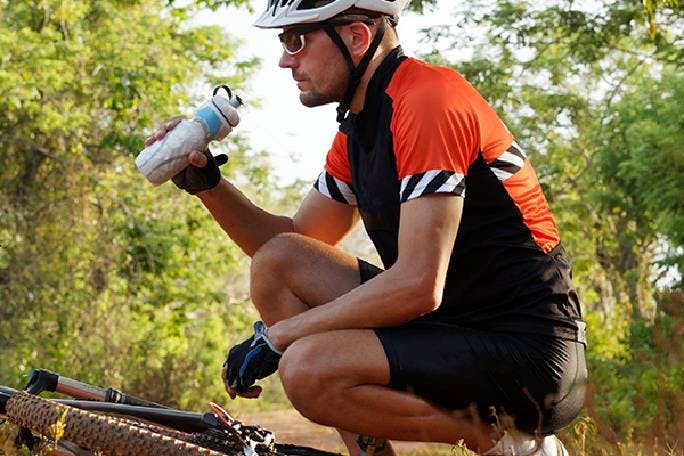 Man drinking water while crouching  near bicycle 