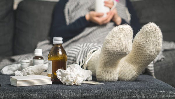 Sick person wearing woolen socks and drinking warm beverage