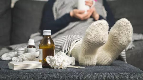 Sick person wearing woollen socks and drinking warm beverage 