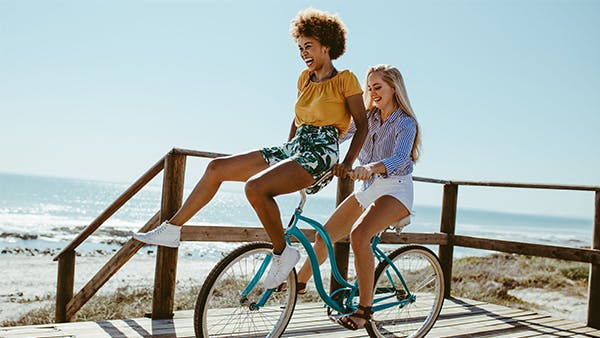 Two women riding a bike by the beach 