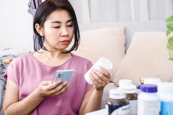 Woman examines the contents of dietary supplements she has at home to identify which vitamins to take together.