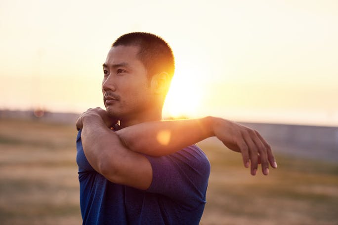 focused athletic young Asian man stretching arm