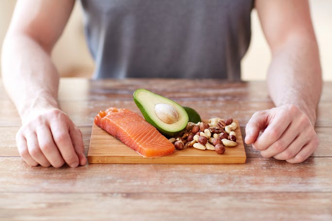 person seated at a table with fish, avocado and nuts  