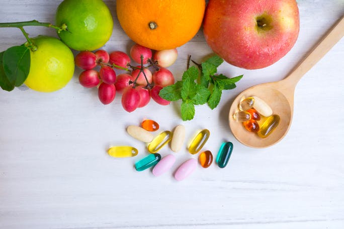 vitamin capsules in a wooden spoon next to fruits 