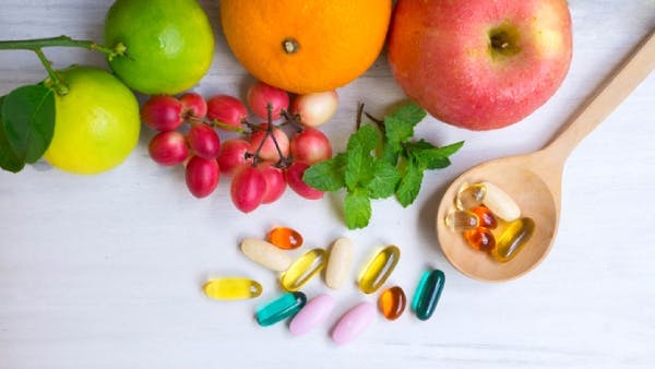 vitamin capsules in a wooden spoon next to fruits