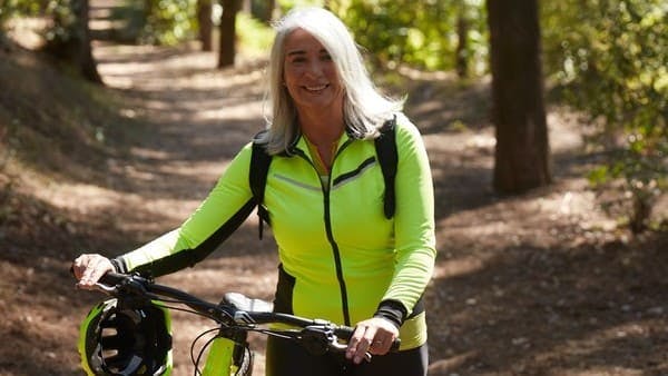 middle aged woman in neon workout gear with bike on a trail