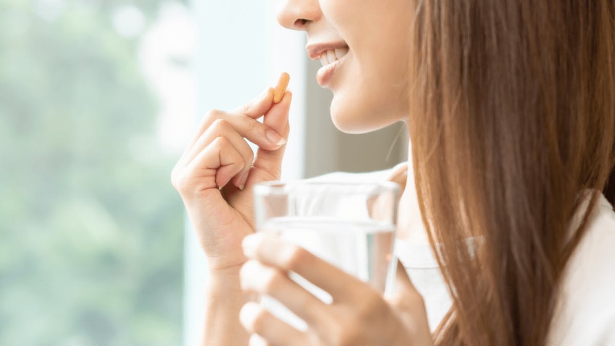 Woman holding vitamin to mouth with glass of water