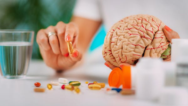 Woman holding a pill capsule and a brain model. 