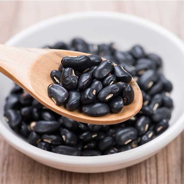 Black beans on a wooden spoon with ceramic bowl