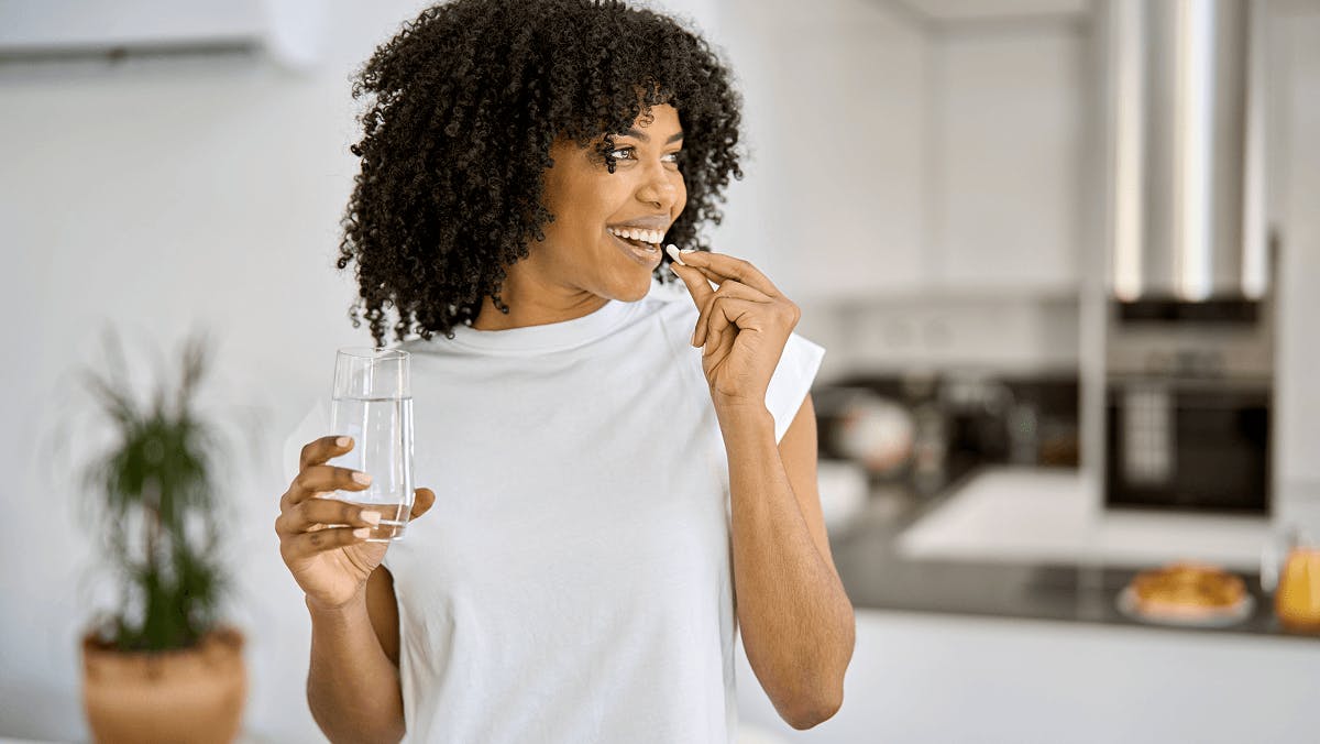 A woman taking a supplement pill with a glass of water in her hand