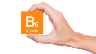 A hand holds an orange card with the text “B6 Vitamin”