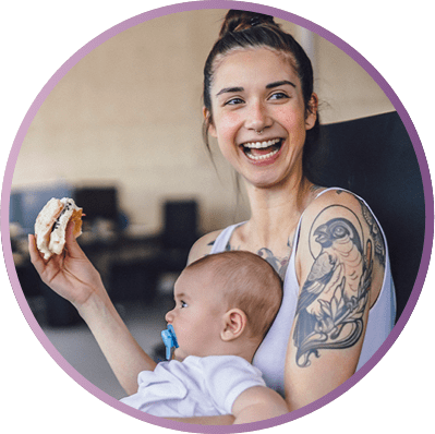 Mamá sonriendo sostiene a su bebé y un sandwich