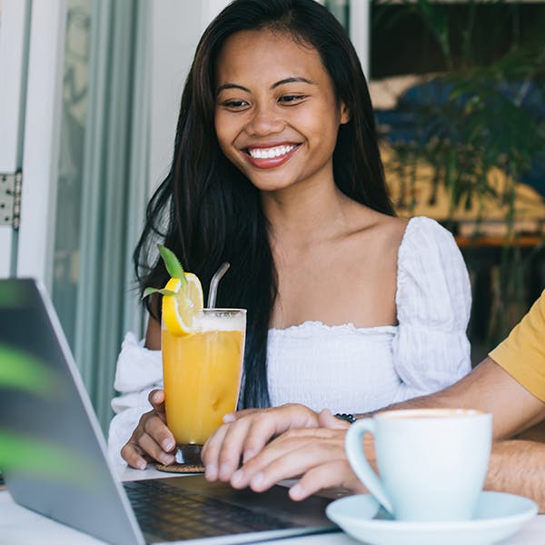 Smiling woman holding a drink looking at a laptop 