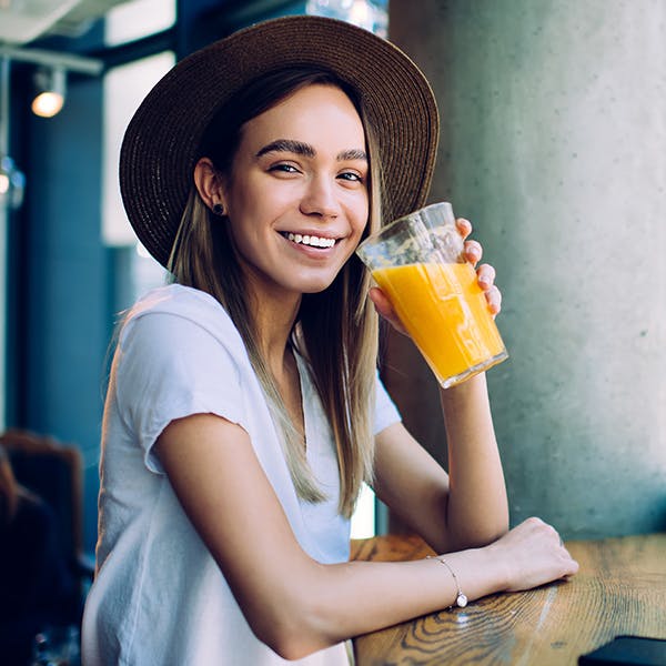 Smiling woman with a hat on drinking an orange drink 