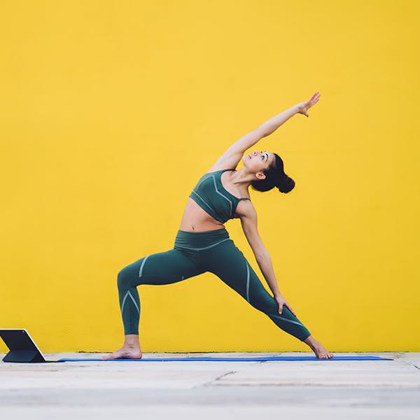 Woman doing yoga stretches in exercises clothes on a yellow background