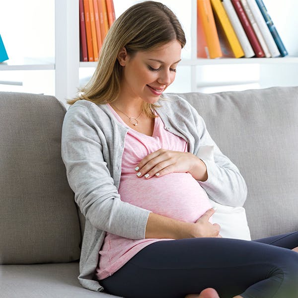 Pregnant woman sitting on a couch touching her stomach