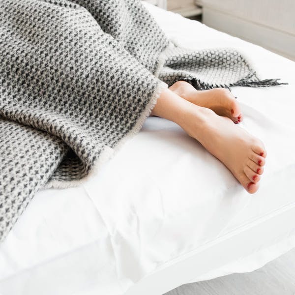 Feet under grey blanket in bed