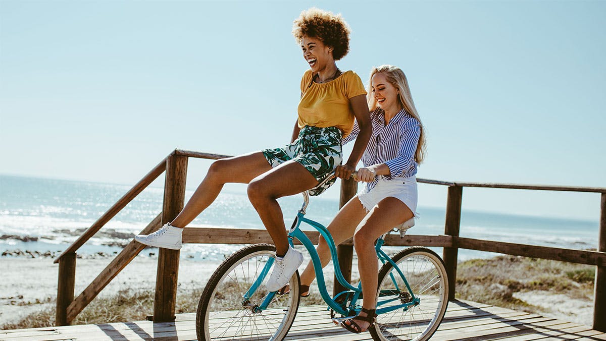 Two women riding a bike by the beach