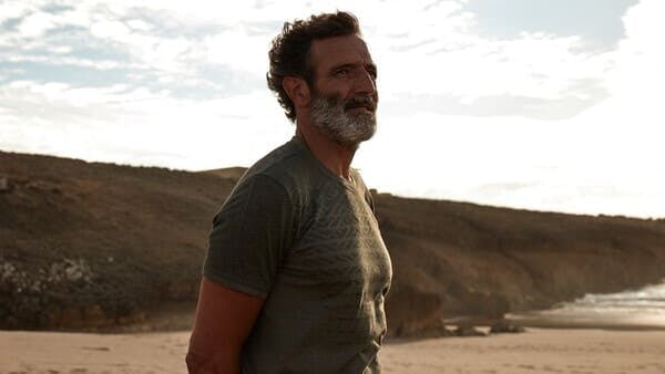 middle aged man with grey beard wearing a t shirt on a beach