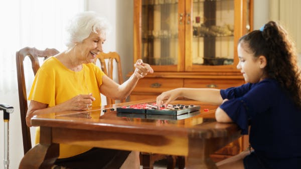Happy little girl playing checkers with senior woman at home
