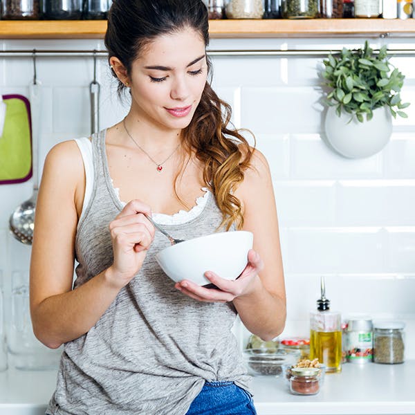 Woman eating a bowl of food in her kitchen 