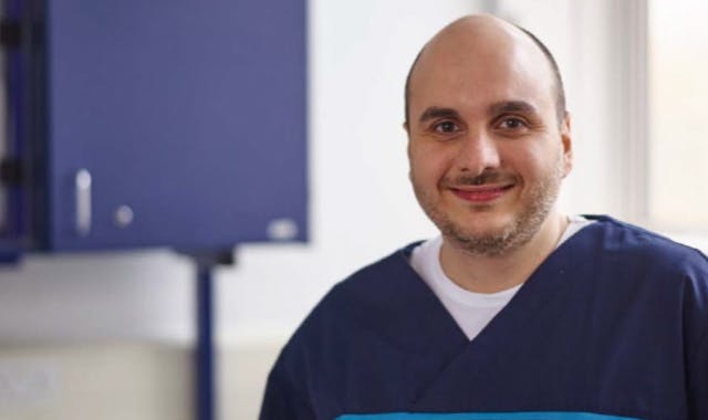 Dentist dressed in scrubs smiles directly at camera