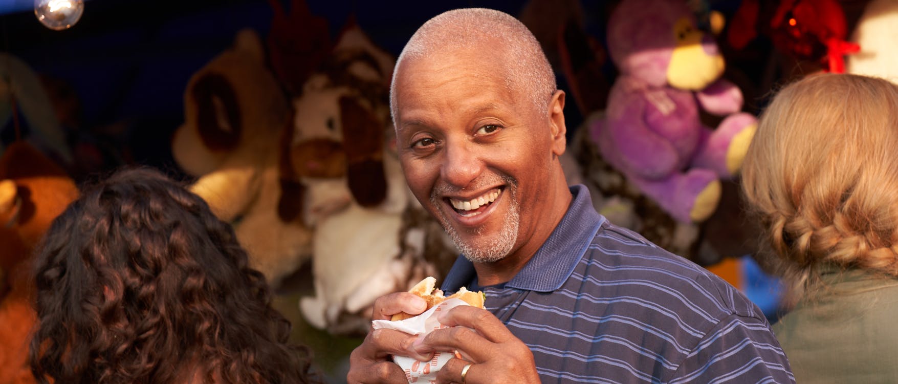 Smiling man holding a partly eaten burger at a town carnival