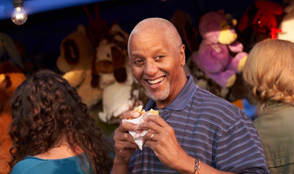 Smiling man holding a partly eaten burger at a town carnival