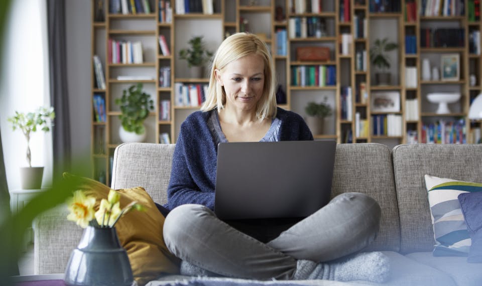 Woman sitting cross-legged on her couch while reading  something on her computer