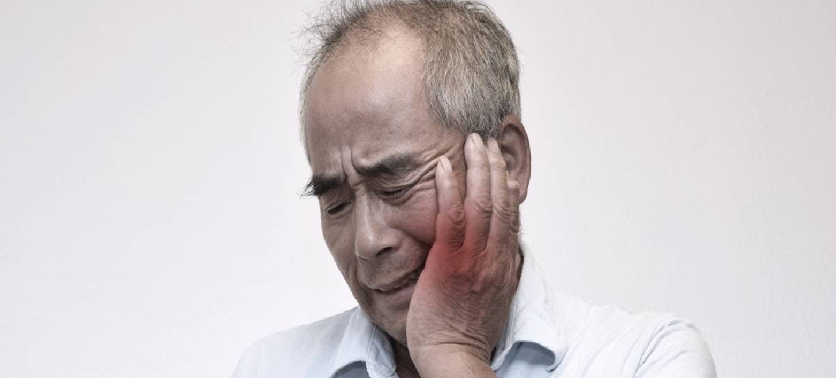 A man holding dentures in one hand with his other hand holding his cheek