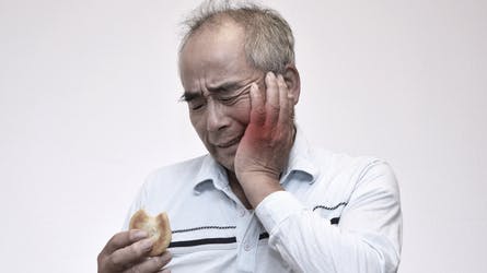 A man holding dentures in one hand with his other hand holding his cheek