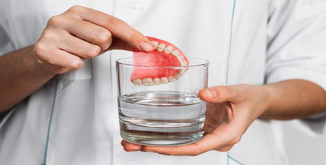 Woman puts dentures into glass of cleaning solution