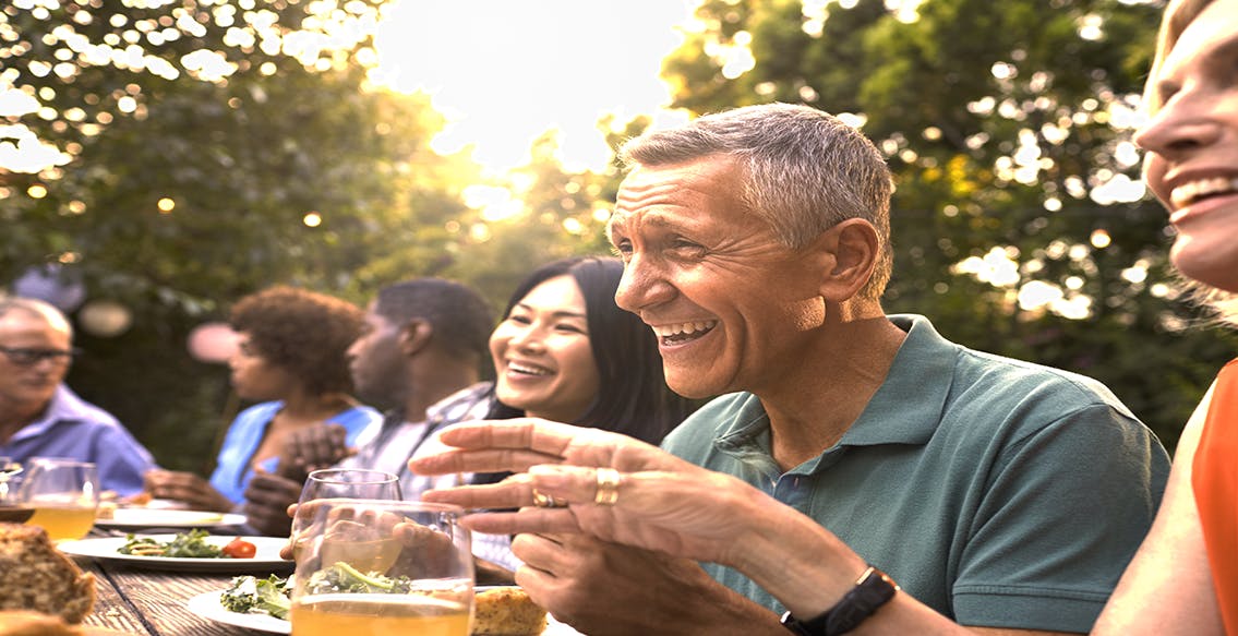 People gathered outdoors at dining table with food and drinks, laughing and talking