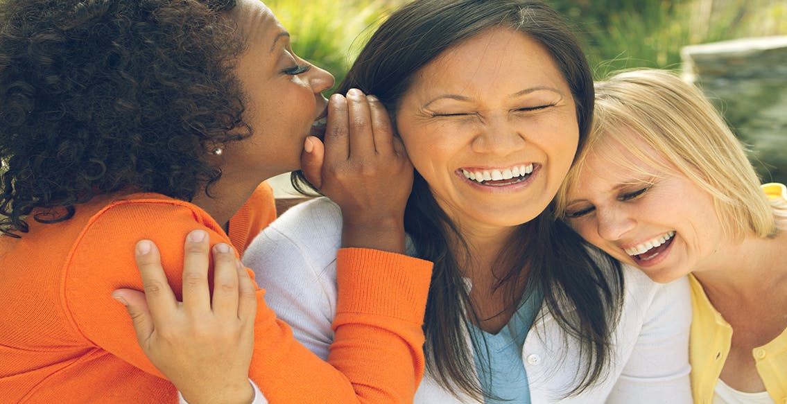 Woman whispering in friend’s ear and women laughing