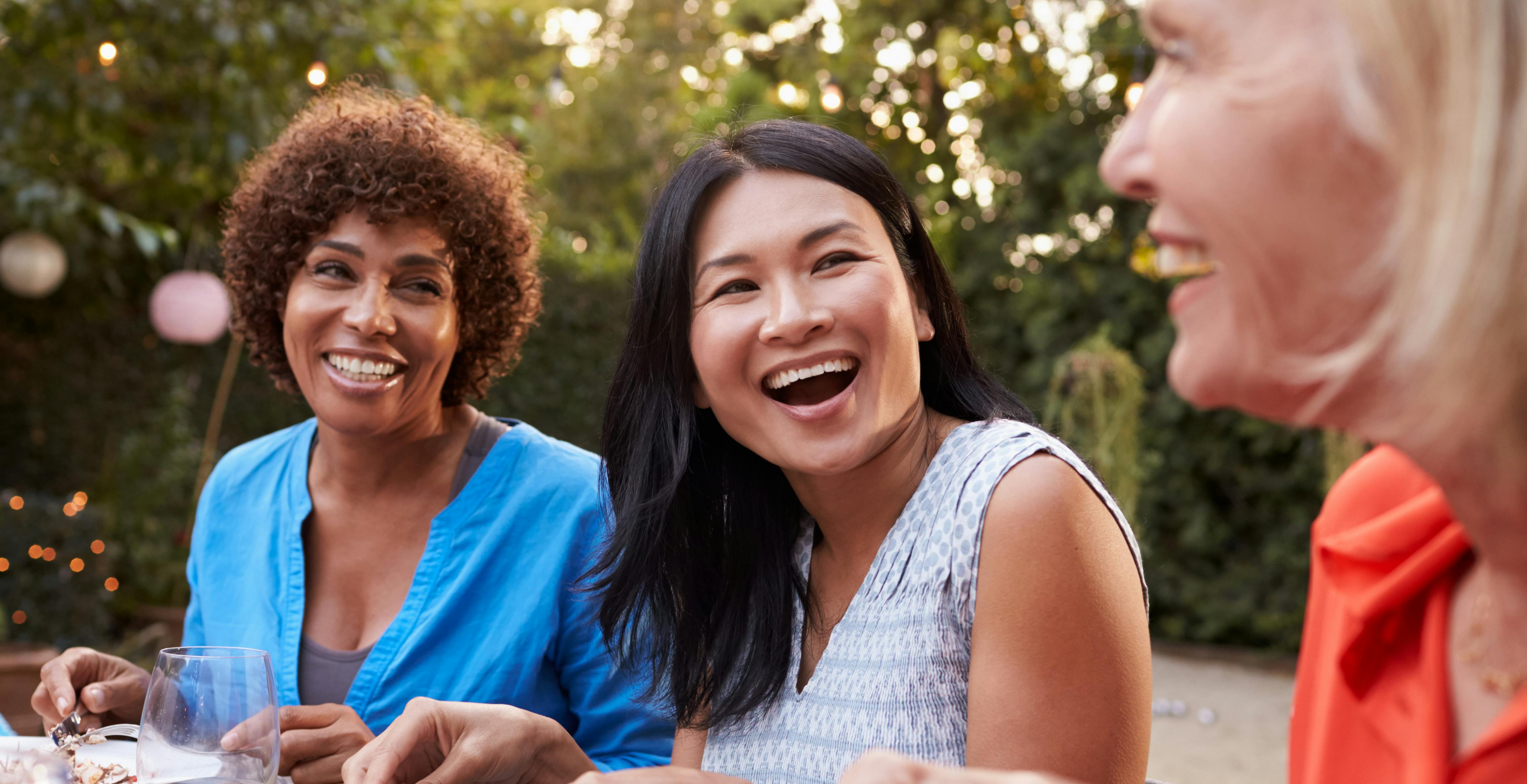 Three women smiling, eating and drinking at table.