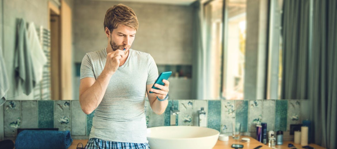 A man brushing his teeth and looking at his phone