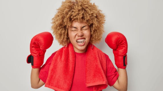 Energized female boxer with curly hair and raised arms wearing boxing gloves and protective mouth guard