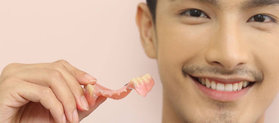Man smiling and holding partial dentures