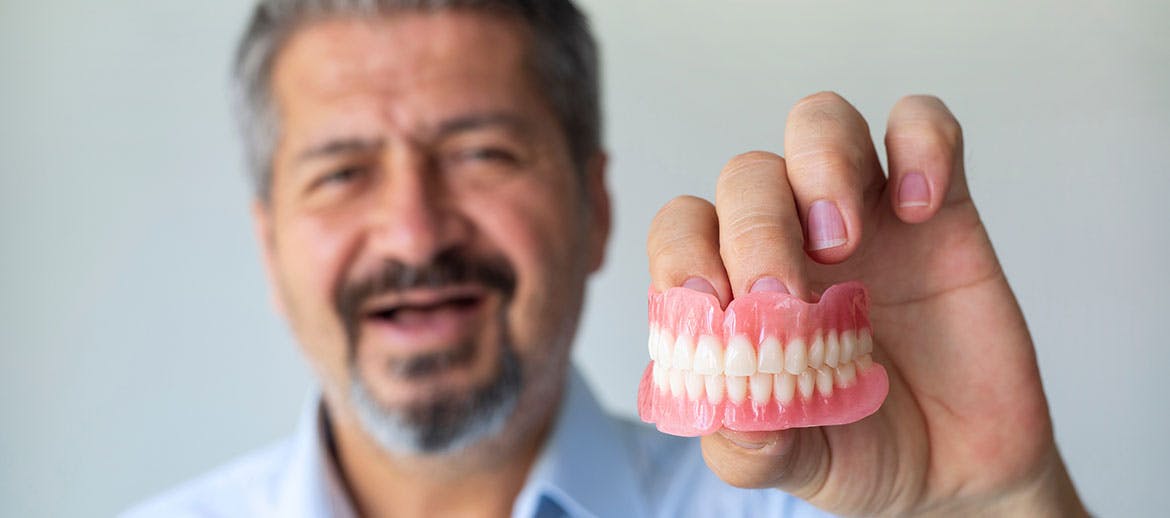 Older man holds dentures in his hand