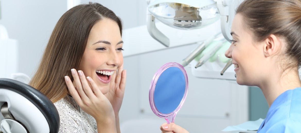 A women smiling into a mirror at the dentist