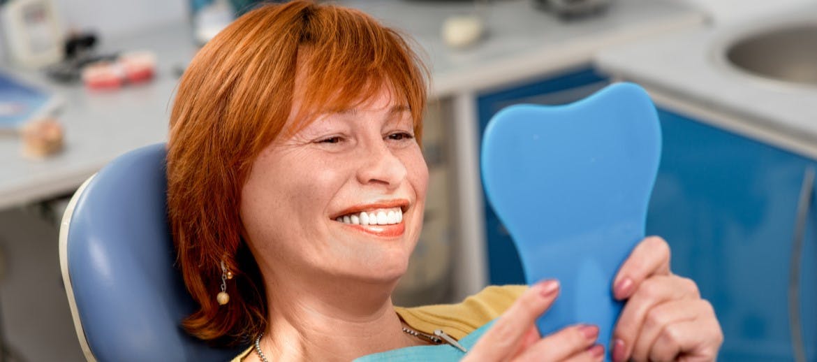 A women smiling into a mirror after having dentures fitted