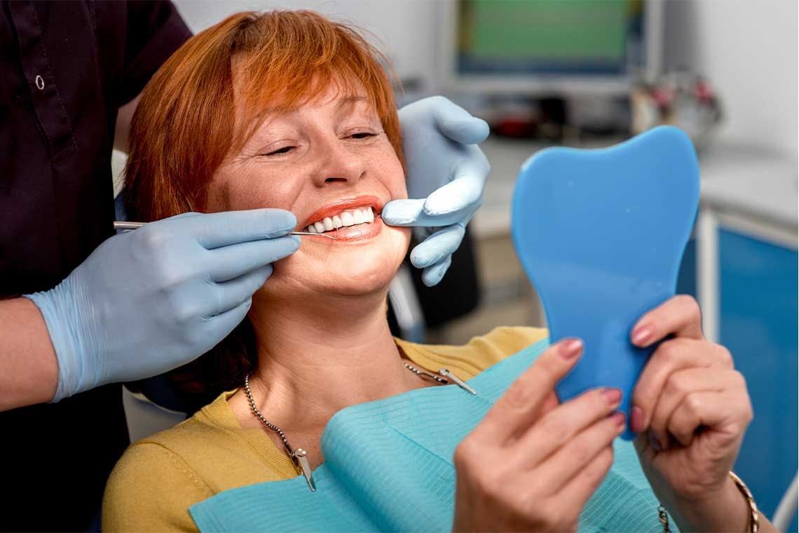 woman with new dental implants looking into the mirror at dental office 