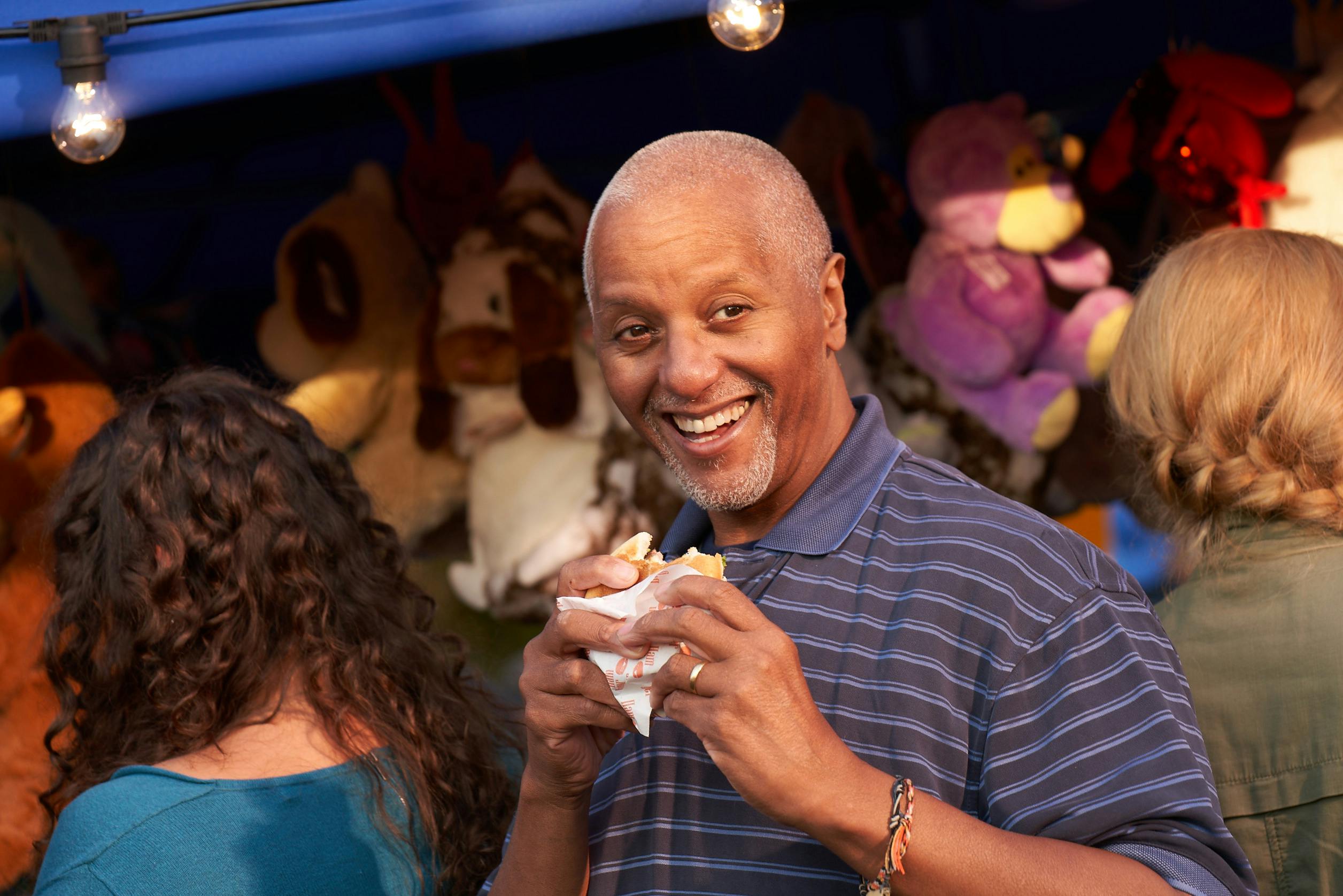 Smiling man holding a partly eaten burger at a town carnival