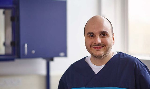 Dentist dressed in scrubs smiles directly at camera