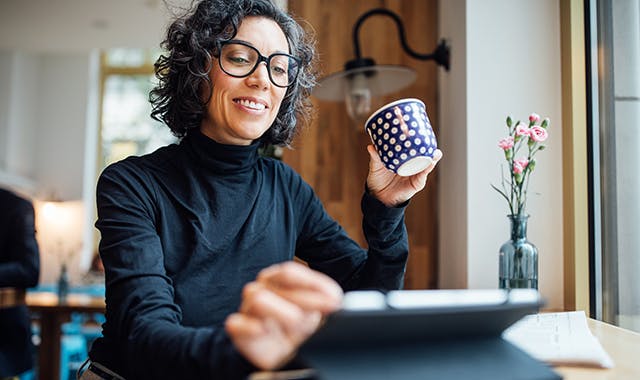 Woman with glasses sitting at a table in her dining  room while looking at her tablet