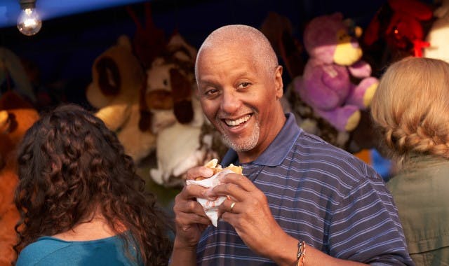 Smiling man holding a partly eaten burger at a town carnival