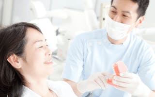 ６０代位の女性が歯医者さんに入れ歯を見てもらっている